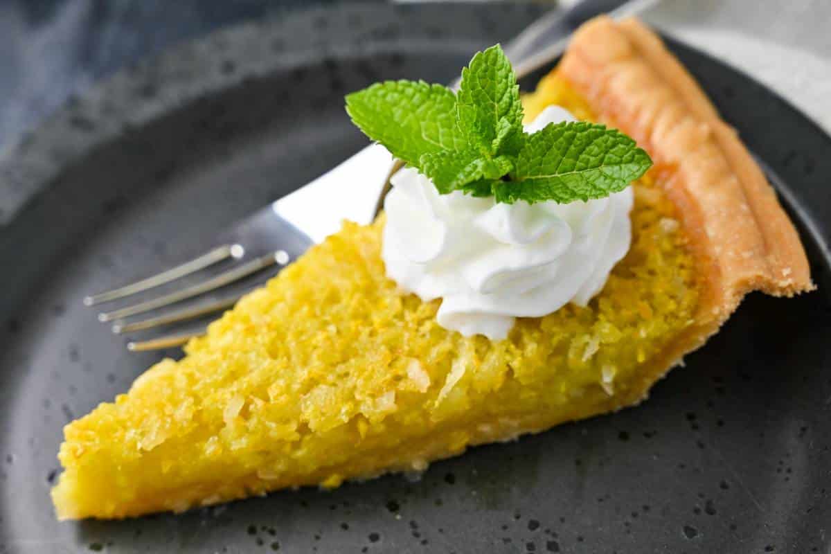 a slice of custard squash pie on a black plate with whipped cream and a sprig of mint