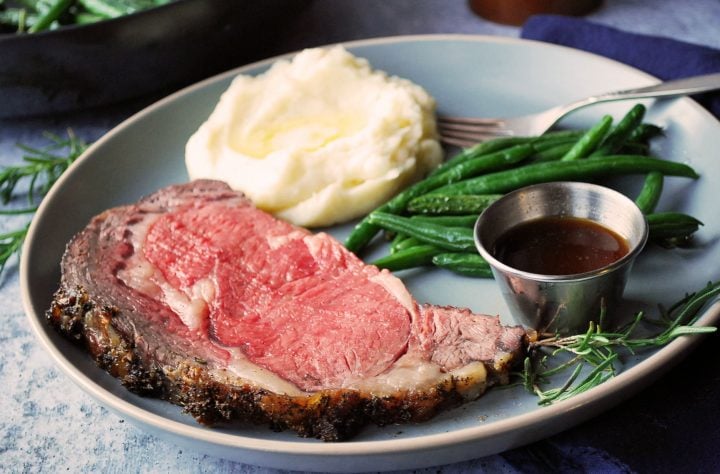 slice of prime rib on a plate with mashed potatoes and green beans