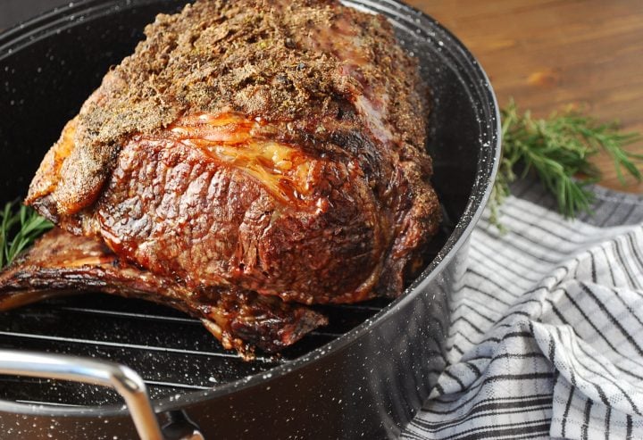 cooked standing rib roast in a roasting pan on a striped towel
