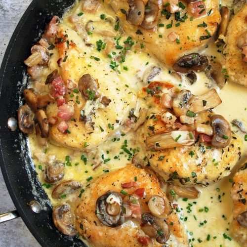 overhead photo of skillet with cooked chicken breasts in a tarragon cream sauce with mushrooms