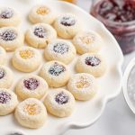 jam filled thumbprint cookies on a platter with jam in background