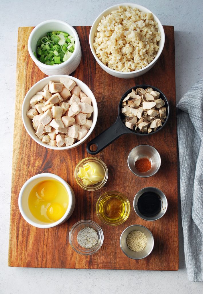 ingredients for chicken fried rice in bowls on top of a wooden cutting board