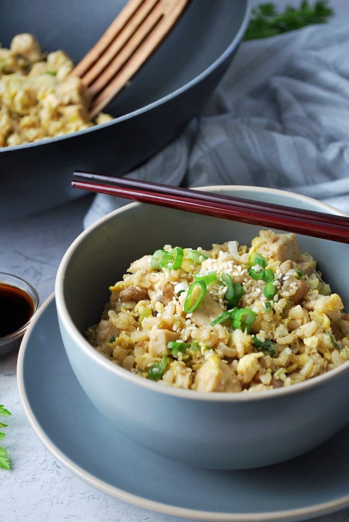 skillet of fried rice with a wooden spoon and a bowl of fried rice with sauce and chopsticks
