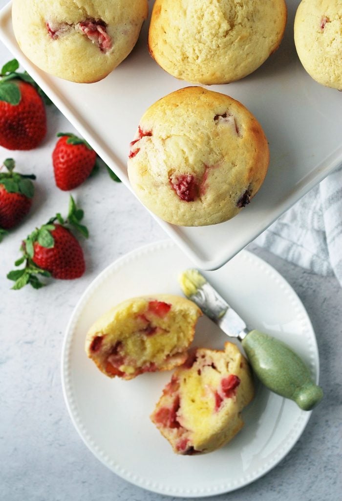 muffins on a white platter with a sliced buttered muffin on a plate with a butter knife