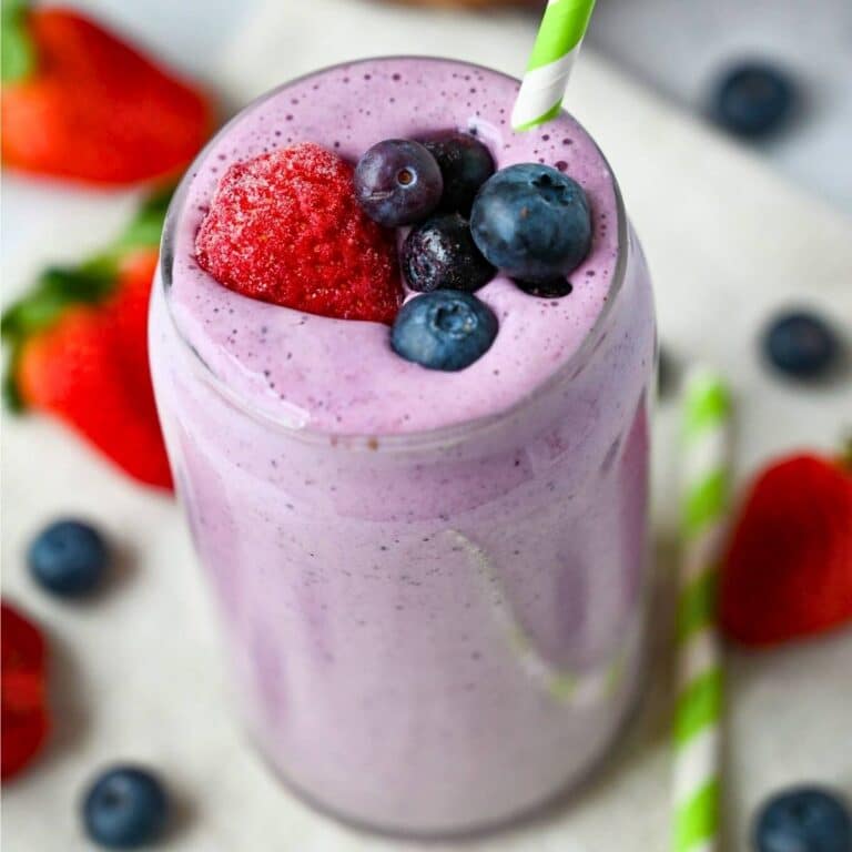 a berry bliss smoothie with blueberries and a frozen strawberry on top with berries around it