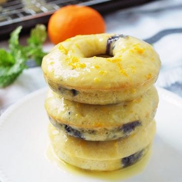 stacked blueberry donuts on a plate dripping with orange glaze