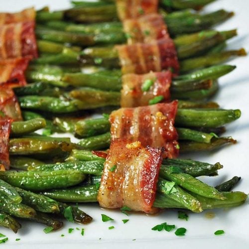 close up photo of cooked bacon-wrapped green beans on a platter with chopped parsley on top