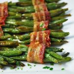 Close up photo of roasted green bean bacon bundles on a white platter with a napkin and fork on the side