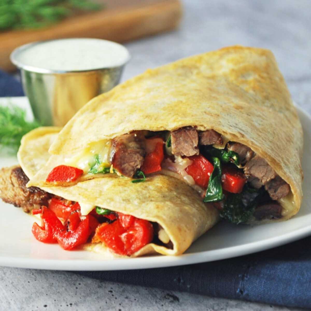 sliced steak quesadilla on a white plate with a cup of dipping sauce