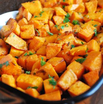 close up photo of roasted sweet potatoes topped with fresh parsley in a casserole dish
