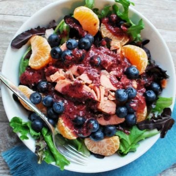 overhead photo of a salad topped with salmon, blueberries, orange slices and blueberry dressing