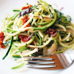 close up of a spiralized zucchini salad with olives and sun-dried tomatoes
