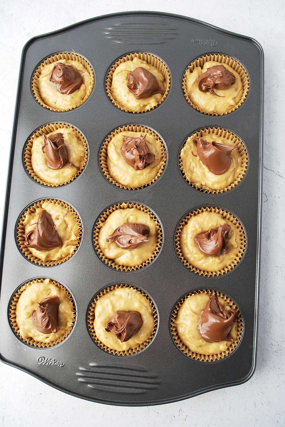 pan of muffin batter in cupcake liners with a dollop of Nutella on top