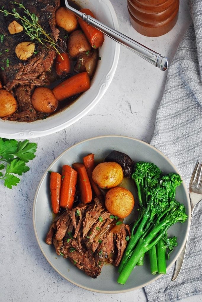 overhead photo of plated pot roast with vegetables and a serving dish of pot roast with a napkin on the side.
