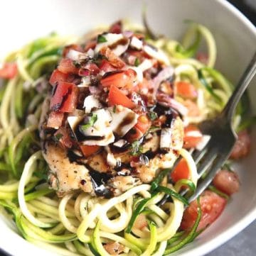 a bowl of zucchini noodles topped with chicken, tomatoes, and sauce