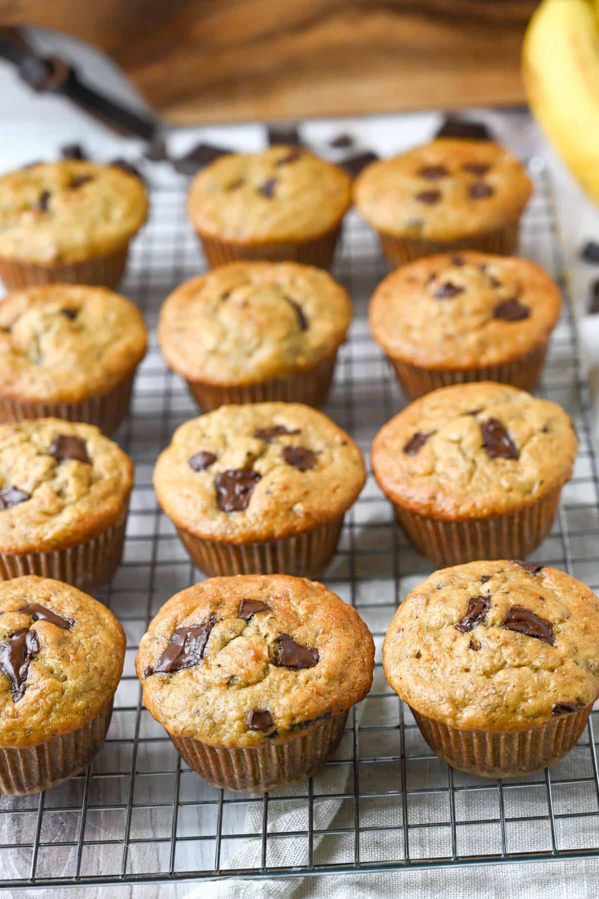banana muffins with chocolate pieces throughout on a cooling rack next to bananas