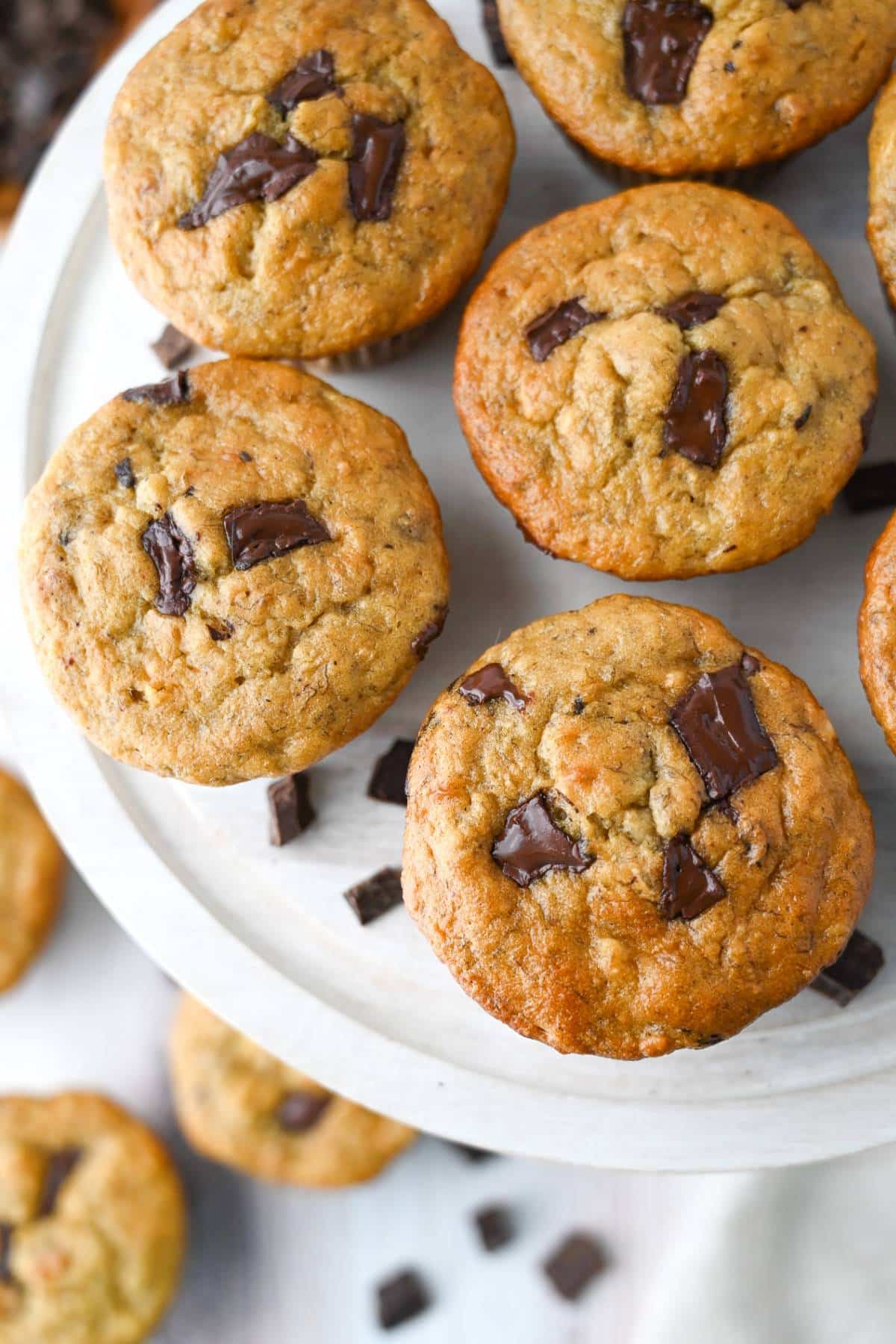 looking down at a platter of chocolate chunk muffins with muffins around it below with chocolate pieces around them