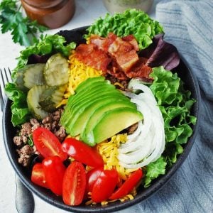 close up of a California burger bowl topped with avocado, tomatoes, pickles, bacon, onions, and cheese