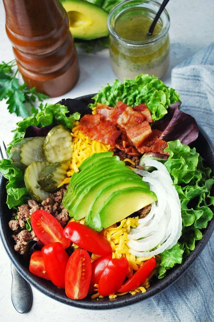 burger bowl topped with ranch vinaigrette, avocado, and a peppermill in the background