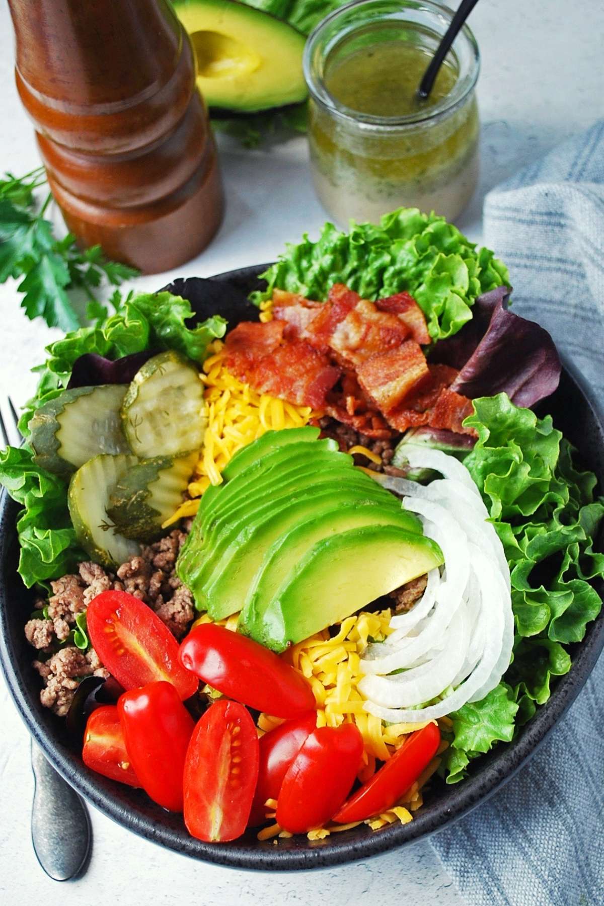 burger bowl topped with ranch vinaigrette, avocado, and a peppermill in the background