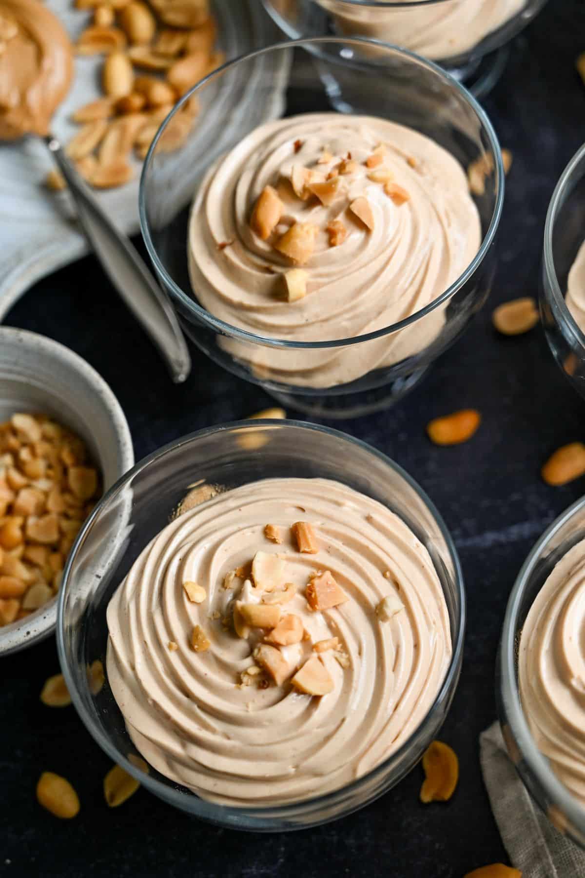 peanut butter mousse piped into dessert glasses with chopped peanuts on top with a dish of peanuts next to it