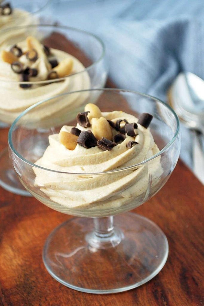 close up of peanut butter mousse in a clear parfait glass topped with chocolate and peanuts
