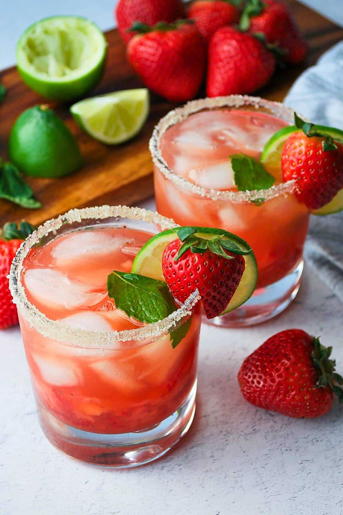two strawberry mojitos with mint, lime and a strawberry on the rim