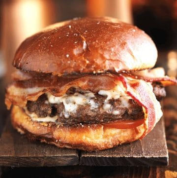 close up of a smoked burger with white cheese and bacon on a brioche bun