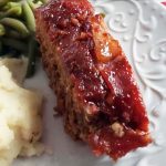 smoked meatloaf with a glaze on a plate with mashed potatoes and green beans