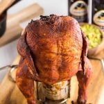 whole smoked chicken on a beer can with bottles of beer in the background