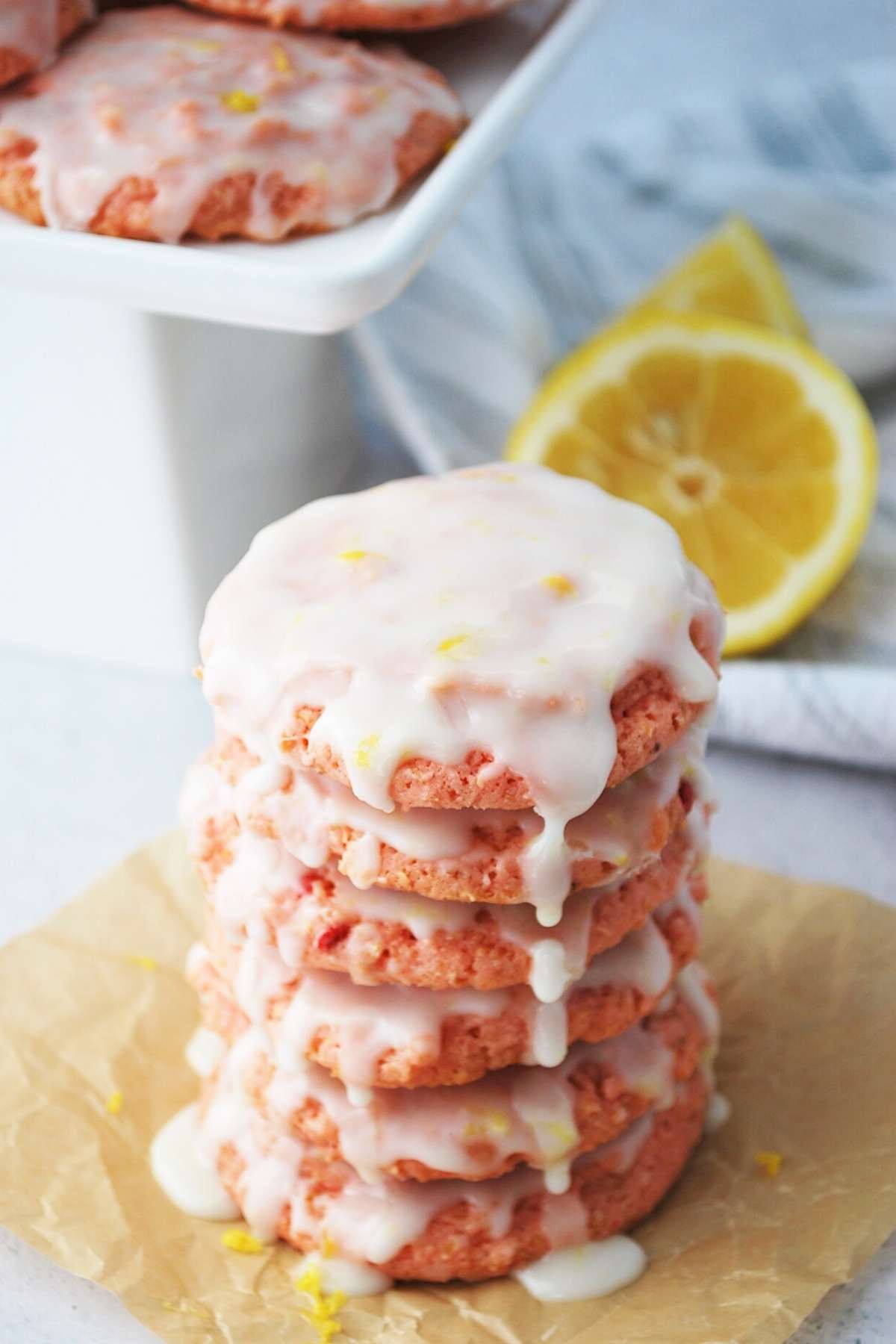 stack of strawberry lemonade cookies dripping with glaze with a platter of cookies in the background