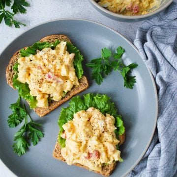 egg salad on toast on a plate with sprigs of parsley