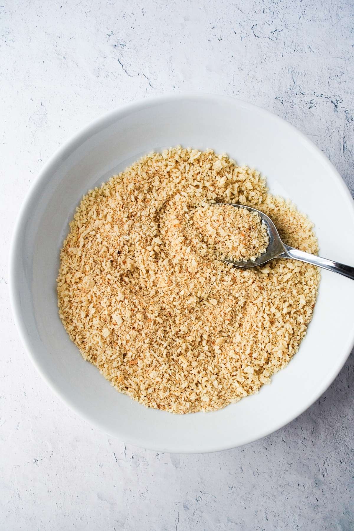Breadcrumbs in a white bowl with a spoon
