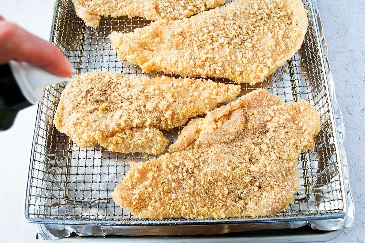 chicken cutlets getting sprayed with cooking oil in an air fryer