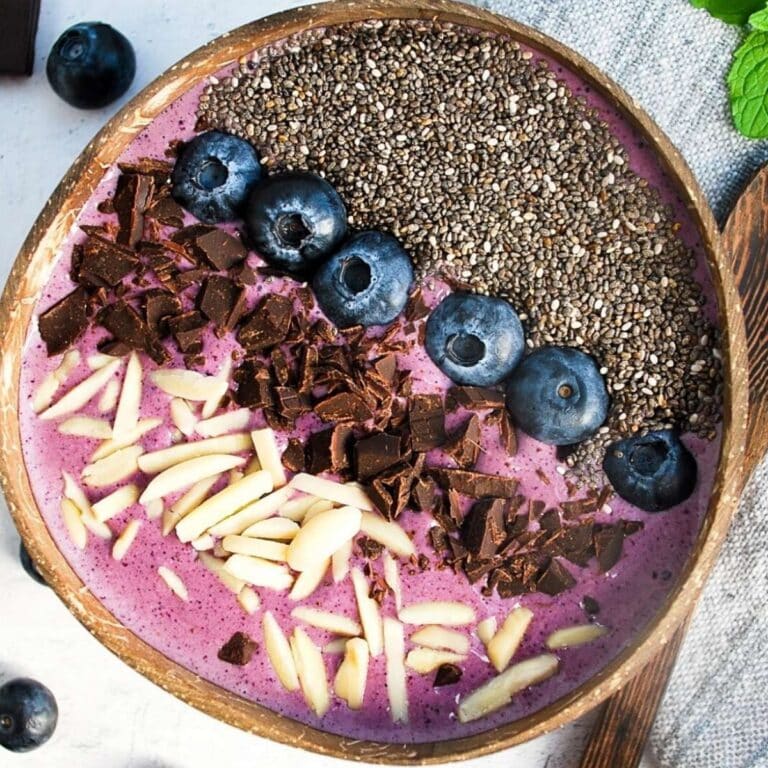 looking down at a blueberry smoothie bowl with almonds, cacao nibs, fresh blueberries, and chia seeds on top