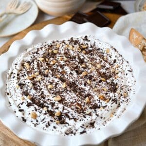 chocolate hazelnut pie in a white pie pan with chocolate shavings and chopped hazelnuts on top of a cool whip topping