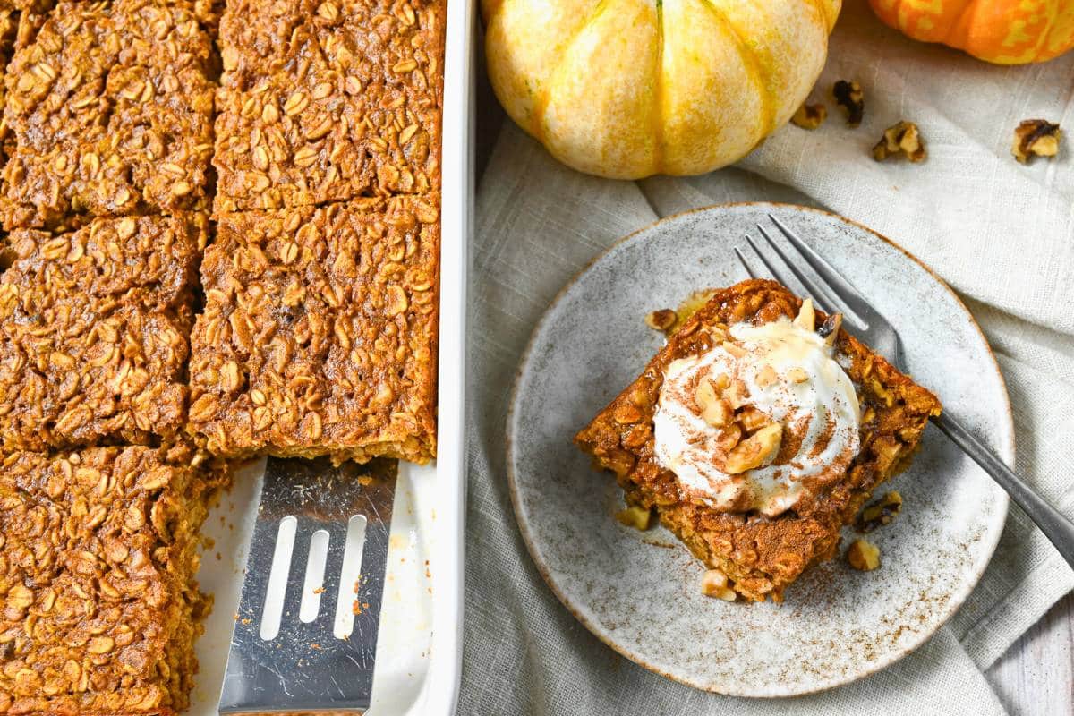 a sliced pan of baked oats with a plated serving next to it and mini pumpkins around it