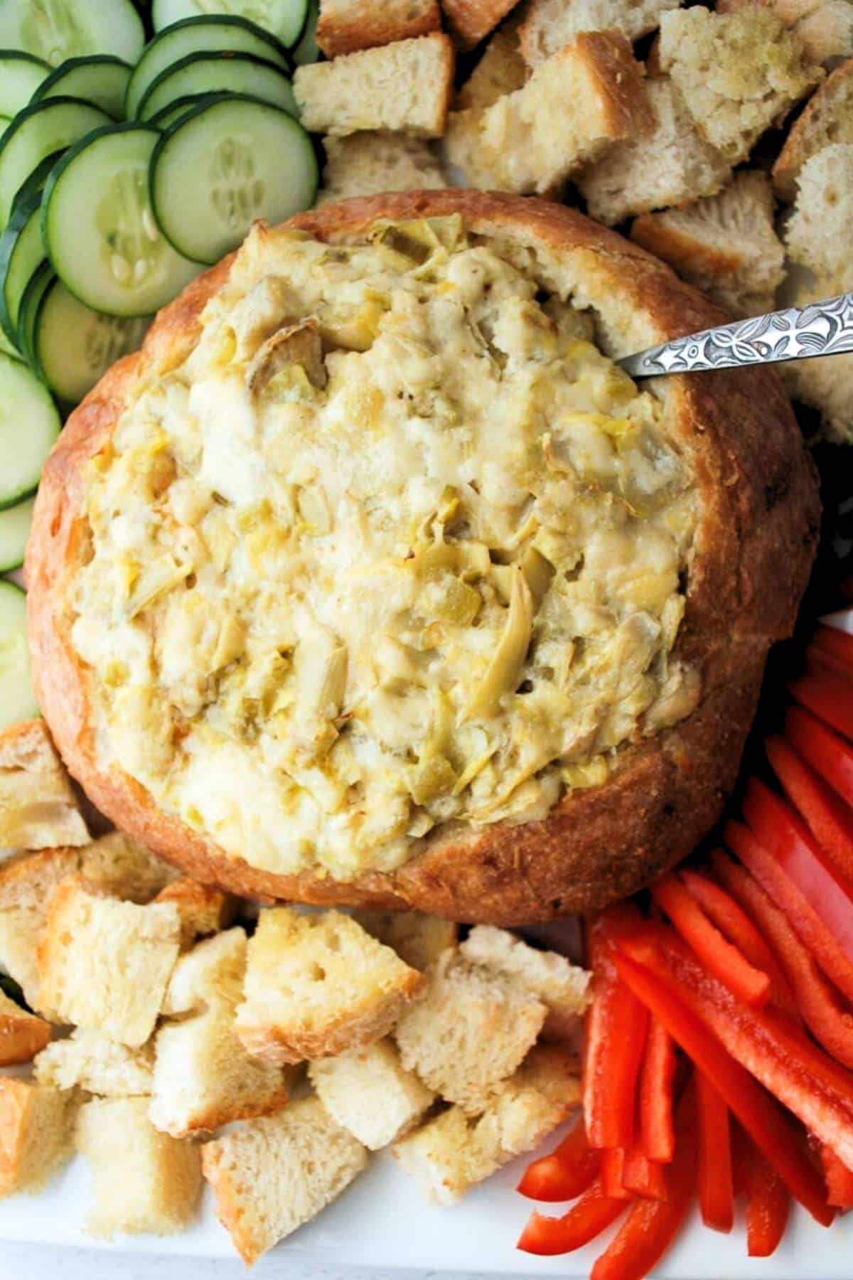 artichoke dip with jalapenos and parmesan in a bread bowl with veggies