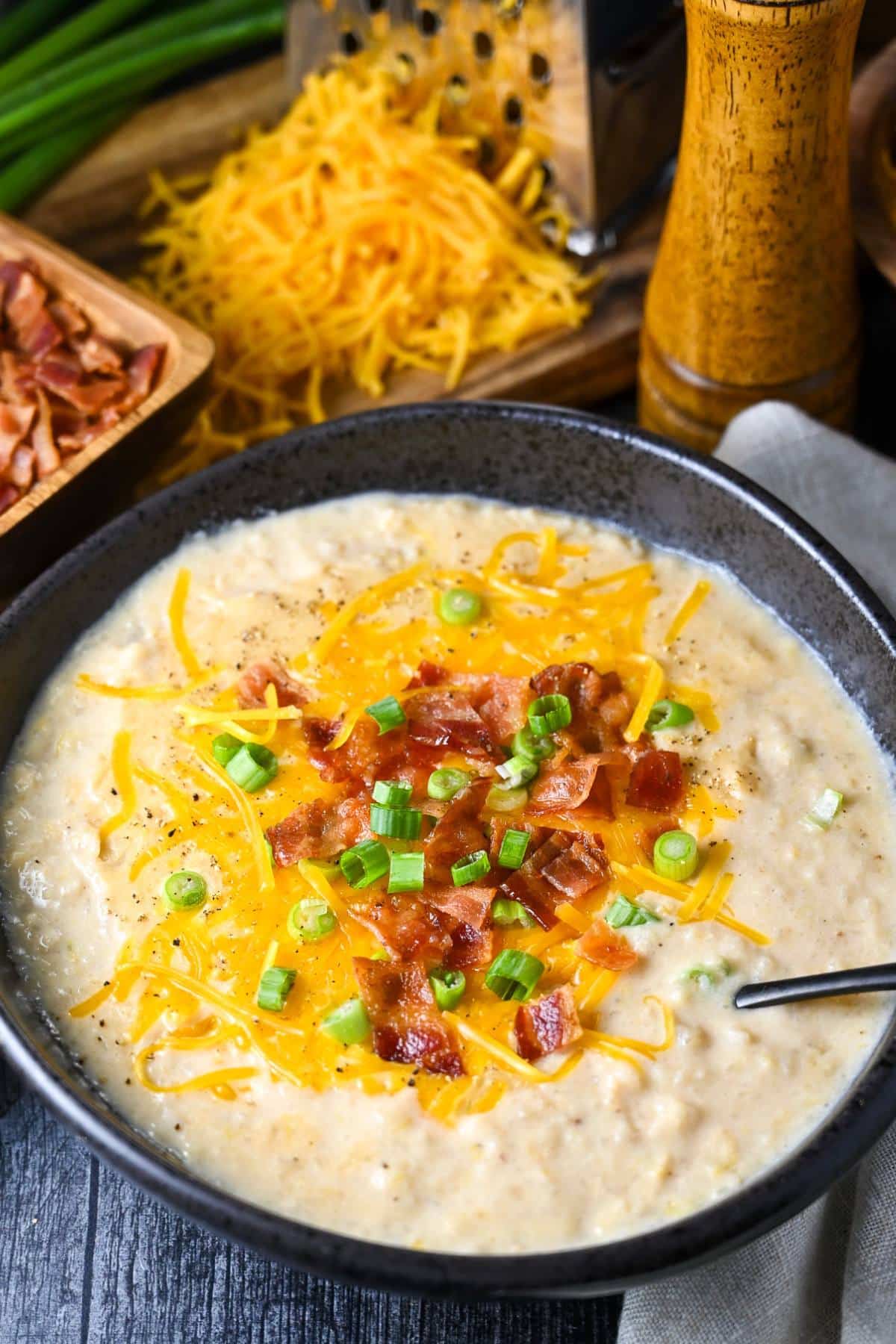 a bowl of potato leek soup with toppings and a bowl of bacon and shredded cheese behind it