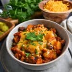 close up of butternut squash chili with beef in a bowl with cheese and cilantro garnish
