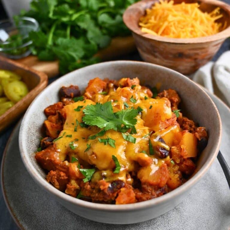 close up of butternut squash chili with beef in a bowl with cheese and cilantro garnish