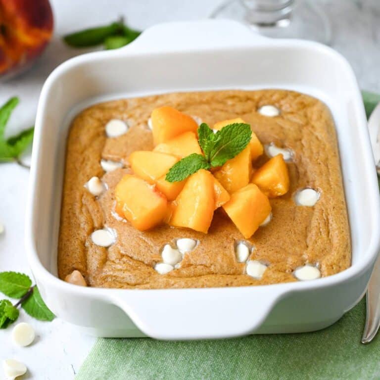 side view of a white baking dish with cake-like baked peach oats with sliced peaches and white chocolate chips