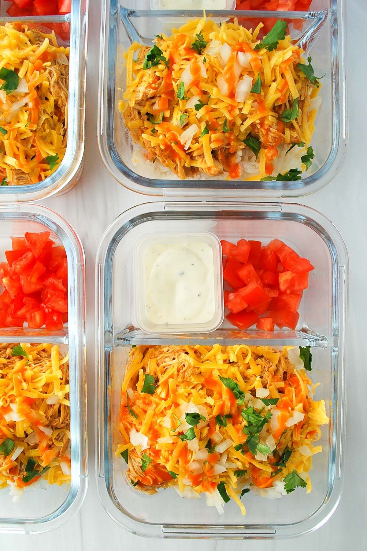 shredded buffalo chicken over rice in meal prep bowls with tomatoes and ranch
