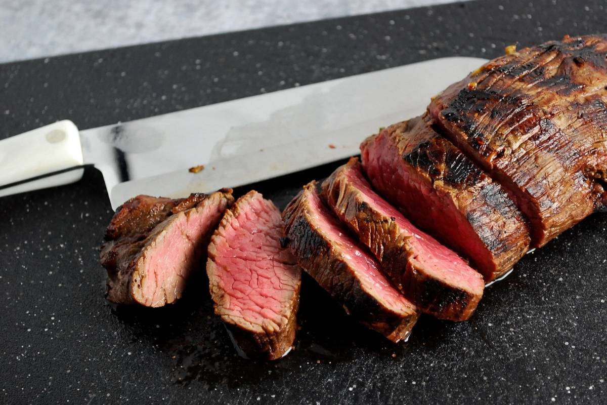 sliced Teres Major steak on a cutting board with a knife