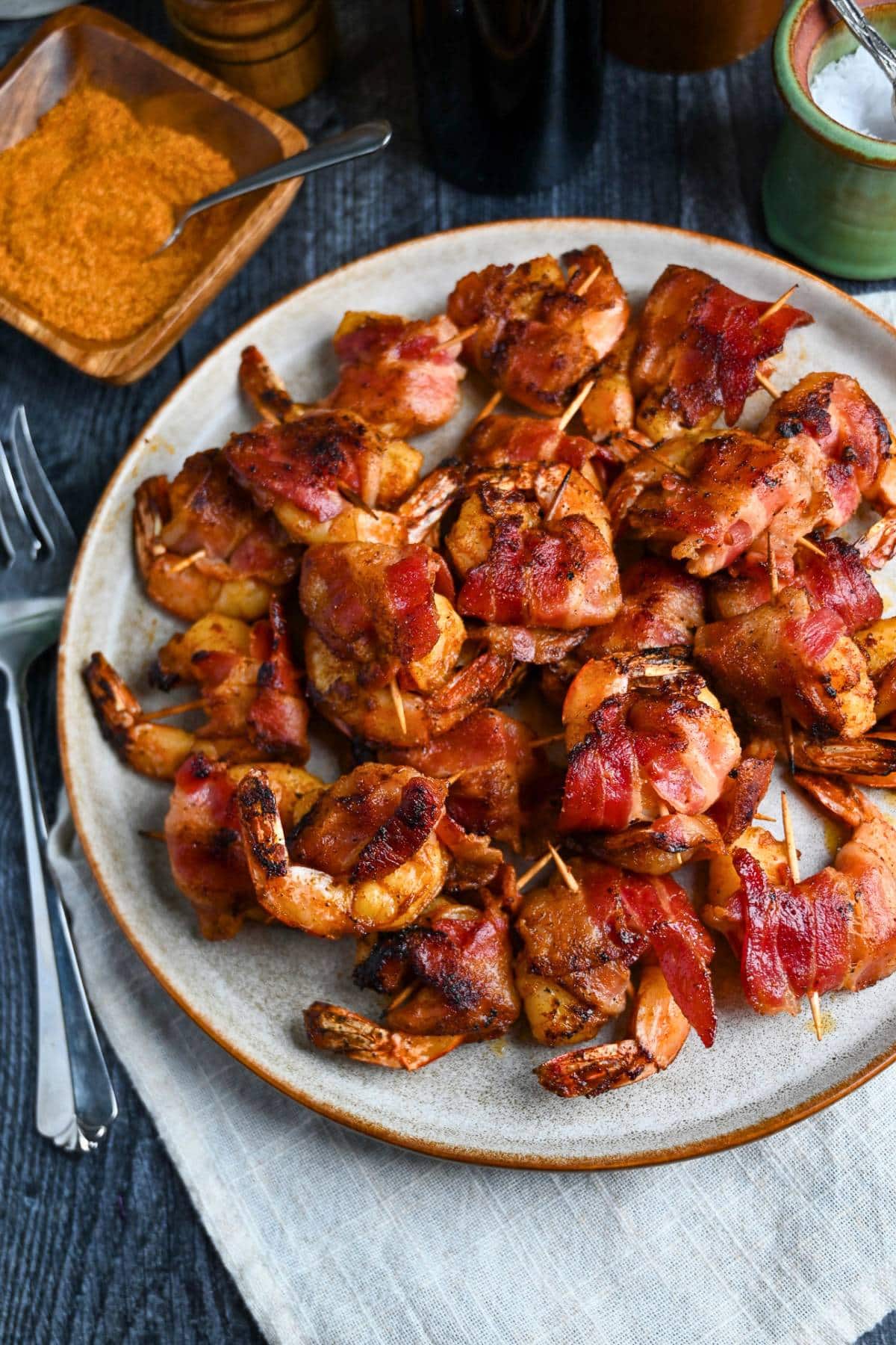 a plate of grilled bacon wrapped shrimp with a bowl of adobo seasoning next to it
