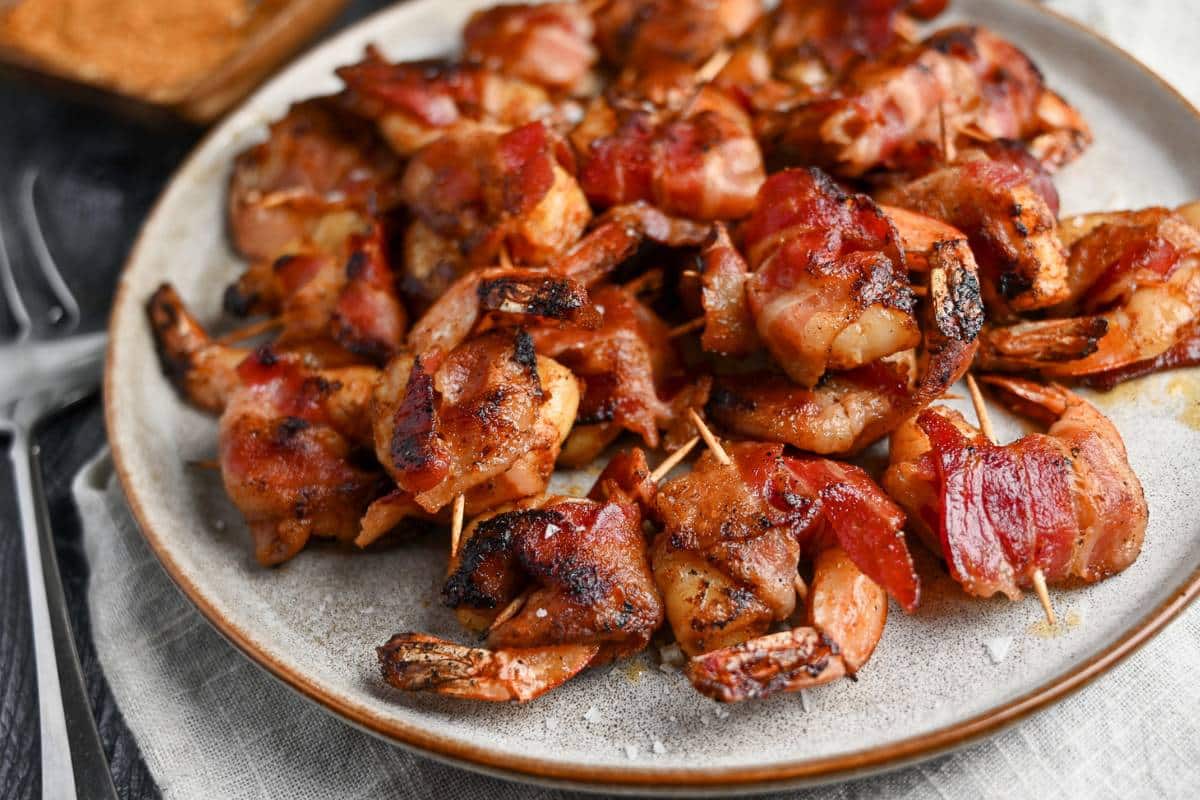 side view of a platter of grilled shrimp wrapped in bacon with a toothpick 