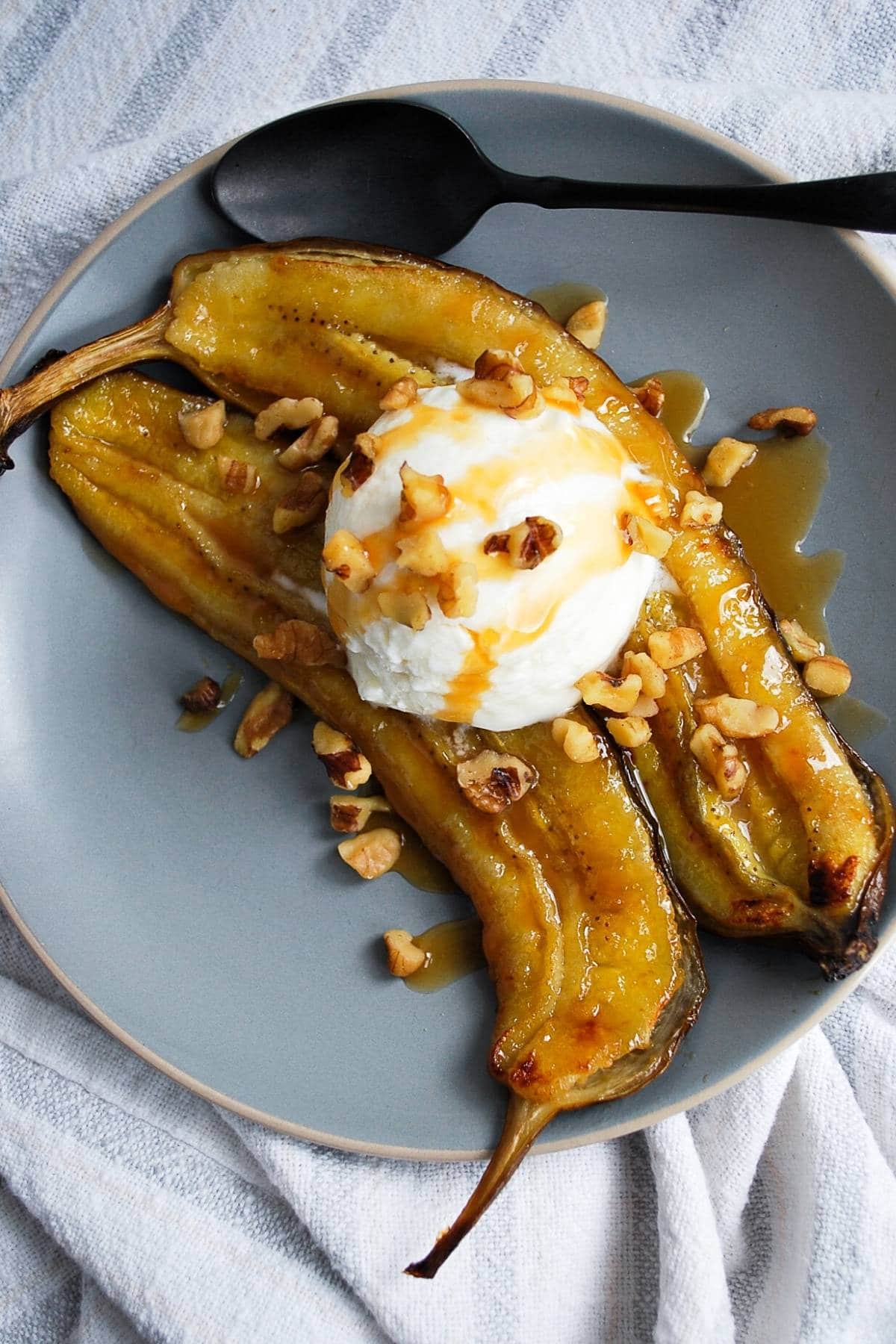 an air fryer banana topped with frozen greek yogurt, walnuts and caramel syrup on a plate with a spoon