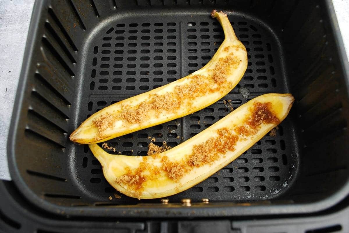 sliced banana topped with butter and coconut sugar in an air fryer basket ready to cook