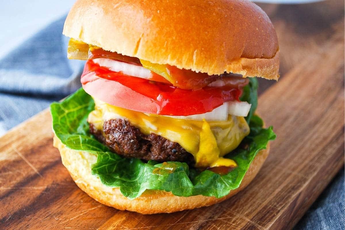 side view of a juicy burger with all the toppings on a brioche bun on a cutting board