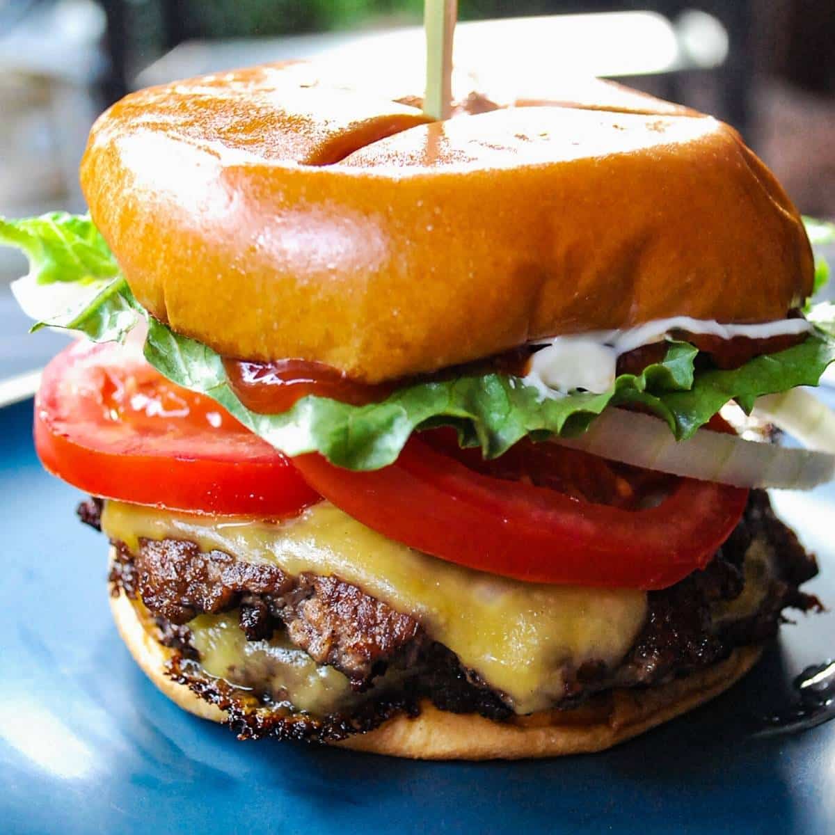 close up of a loaded smash burger on a plate outside near a Blackstone griddle